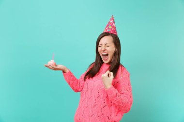 Genç kadında çok memnun: örgü pembe kazak Doğum günü şapkası kenetlenmesi yumruk kazanan gibi çığlık tutun el pasta üzerinde mavi arka plan izole mum ile. İnsanlar yaşam tarzı kavramı. Kopyalama alanı alay