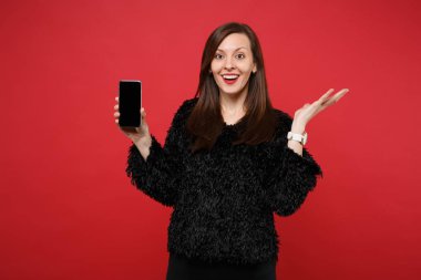 El yayılan, parlak kırmızı zemin üzerine izole boş boş ekran ile cep telefonu tutarak siyah kürk kazaklı genç kadın hayran. İnsanlar samimi duygular, yaşam kavramı. Kopyalama alanı alay
