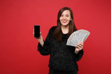 Excited young woman holding mobile phone with blank empty screen fan of money in dollar banknotes cash money isolated on red background. People sincere emotions, lifestyle concept. Mock up copy space