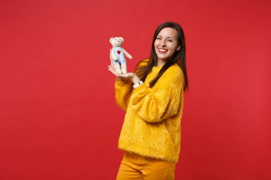 Tutmak oyuncak ayı peluş oyuncak parlak kırmızı duvar arka planda Studio izole sarı kürk kazaklı neşeli genç kadın portresi. İnsanlar samimi duygular, yaşam kavramı. Kopyalama alanı alay