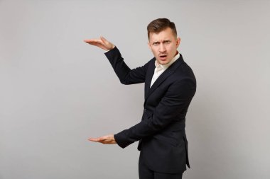 Söz konusu genç iş adamı klasik siyah takım elbise gri duvar arka plan üzerinde izole dikey kopya alanı ile boyutu gösteren el hareketi. Başarı kariyer servet iş kavramı. Reklam alanı