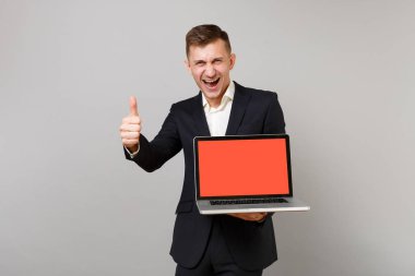 Mutlu genç iş adamı siyah giyin gösteren başparmak, dizüstü pc bilgisayar boş boş ekran gri arka plan üzerinde izole ile tutarak. Başarı kariyer servet iş kavramı. Kopyalama alanı alay