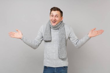 Neşeli genç adam gri süveterli Yayilim eller gri duvar arka planda, stüdyo portre izole eşarp. Sağlıklı moda yaşam tarzı insanların samimi duygular, soğuk sezon kavramı. Kopyalama alanı alay