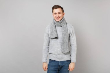 Genç adam gri süveterli gülümseyen portresi, Studio gri duvar arka plan üzerinde duran eşarp izole. Sağlıklı moda yaşam tarzı, insanlar samimi duygular, soğuk sezon kavramı. Kopyalama alanı alay
