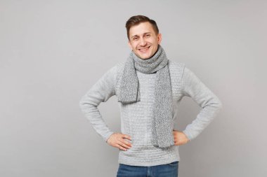 Gri süveterli genç adam gülümsüyor, silah üzerinde gri duvar arka plan üzerinde izole bel akimbo ile ayakta eşarp. Sağlıklı moda yaşam tarzı insanların samimi duygular soğuk sezon kavramı. Kopyalama alanı alay