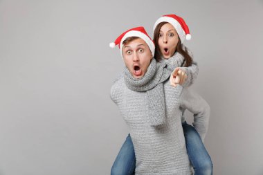 Neşeli eğlenceli çift kız adam Santa Noel şapka gri kazak eşarp gri duvar arka planda, stüdyo portre izole kırmızı. Mutlu yeni yıl 2019 kutlama tatil parti kavramı. Kopyalama alanı alay