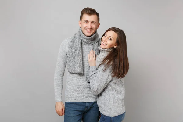 Young cute couple girl guy in gray sweaters, scarves together isolated on grey wall background, studio portrait. Healthy lifestyle, ill sick disease treatment, cold season concept. Mock up copy space