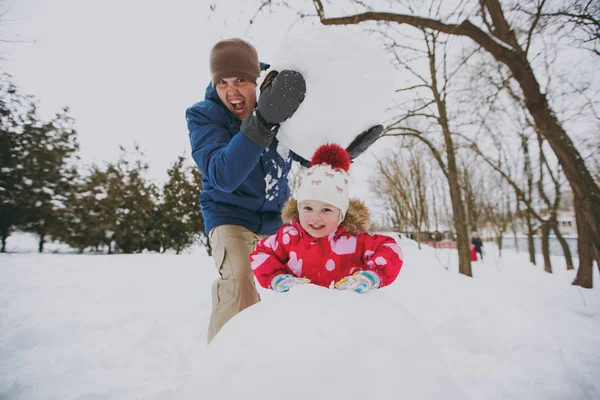 Crazy family screaming dad in warm clothes holding big snowball, little girl playing with snow in park or forest outdoors. Winter fun, leisure on holidays. Love relationship family lifestyle concept