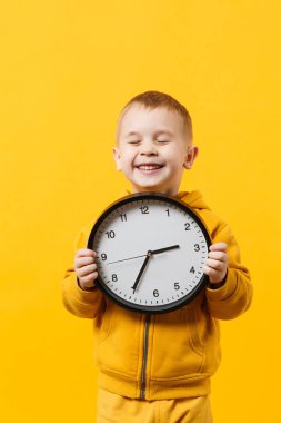 Küçük çocuk çocuk 3-4 yıl sarı elbise giyen eski turuncu duvar arka planda, çocuk stüdyo portre izole saat tutun. İnsanlar samimi duygular, çocukluk yaşam tarzı kavramı. Kopyalama alanı alay