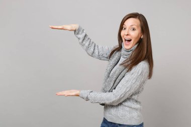 Heyecanlı kız gri kazak atkı gri arka plan üzerinde izole dikey çalışma alanı ile boyutu gösteren işaret içinde. Sağlıklı moda yaşam tarzı insanların duyguları soğuk sezon kavramı. Kopyalama alanı alay