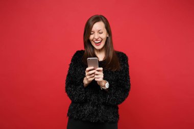 Cep telefonu kullaranarak, parlak kırmızı duvar arka planda Studio izole sms mesajı yazarak siyah kürk kazaklı sevimli genç kadın gülüyor. İnsanlar samimi duygular, yaşam kavramı. Kopyalama alanı alay