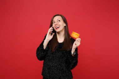 Neşeli genç kadın siyah kürk kazaklı ararken, kredi banka kartı, cep telefonu üzerinde konuşurken tutan izole kırmızı duvar arka plan üzerinde. İnsanlar samimi duygular, yaşam kavramı. Kopyalama alanı alay