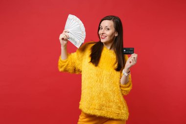 Sarı kürk kazak tutun kredi banka kartı, fan doları banknot, kırmızı zemin üzerine izole para para para gülümseyen genç kadın. İnsanlar samimi duygular yaşam tarzı kavramı. Kopyalama alanı alay