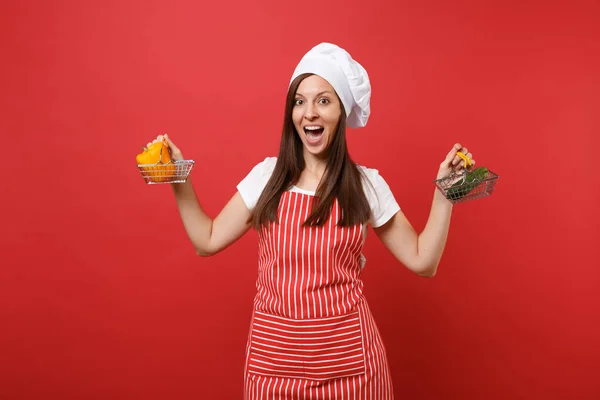 Housewife female chef cook baker in striped apron white t-shirt toque chefs hat isolated on red wall background. Woman hold yellow pepper cucumber in grocery push cart Mock up copy space concept