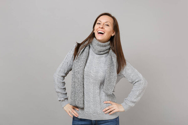 Charming young woman in gray sweater, scarf standing with arms akimbo isolated on grey background in studio. Healthy fashion lifestyle people sincere emotions, cold season concept. Mock up copy space
