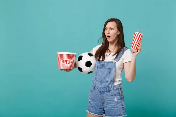 Shocked woman football fan watching match, support favorite team with soccer ball, bucket of popcorn, cup of cola or soda isolated on blue turquoise background. Sport family leisure lifestyle concept
