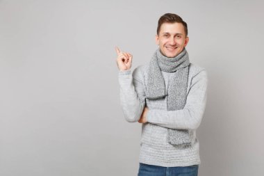 Gri süveterli genç adam gülümsüyor, işaret parmağı kadar izole üzerinde gri arka plan stüdyo eşarp. Sağlıklı moda yaşam tarzı, insanlar samimi duygular, soğuk sezon kavramı. Kopyalama alanı alay