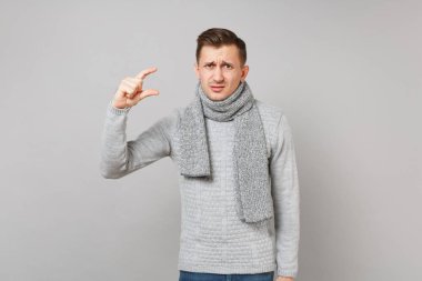 Söz konusu adam gri süveterli eşarp ile gri duvar arka plan üzerinde izole çalışma alanı boyutu gösteren el hareketi. Sağlıklı yaşam, insanlar samimi duygular, soğuk sezon kavramı. Kopyalama alanı alay