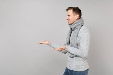 Gri süveterli bir kenara gri duvar arka plan üzerinde izole el işaret eşarp genç adam gülümseyen yan görünüm. Sağlıklı moda yaşam tarzı insanların samimi duygular, soğuk sezon kavramı. Kopyalama alanı alay