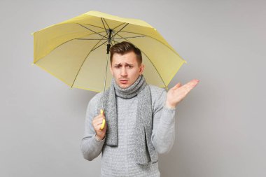 Gri süveterli genç adam üzgün, gri arka plan üzerinde izole el yayılan sarı şemsiye tutan eşarp. Sağlıklı moda yaşam tarzı, insanlar samimi duygular, soğuk sezon kavramı. Kopyalama alanı alay