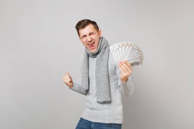 Genç çığlık gri kazak atkı erkekte nakit para kazanan gri arka plan üzerinde izole gibi yumruk kenetlenmesi dolarlık banknotlar demet çok tutun. Sağlıklı yaşam tarzı insanların duyguları soğuk sezon kavramı