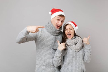 Neşeli eğlenceli çift kız adam Santa Noel şapka gri kazak eşarp gri duvar arka planda, stüdyo portre izole kırmızı. Mutlu yeni yıl 2019 kutlama tatil parti kavramı. Kopyalama alanı alay