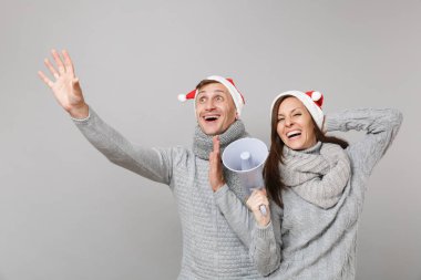 Neşeli eğlenceli çift kız adam Santa Noel şapka gri kazak eşarp gri duvar arka planda, stüdyo portre izole kırmızı. Mutlu yeni yıl 2019 kutlama tatil parti kavramı. Kopyalama alanı alay