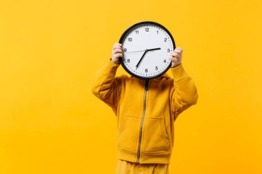 Küçük çocuk çocuk 3-4 yıl sarı elbise giyen eski turuncu duvar arka planda, çocuk stüdyo portre izole saat tutun. İnsanlar samimi duygular, çocukluk yaşam tarzı kavramı. Kopyalama alanı alay