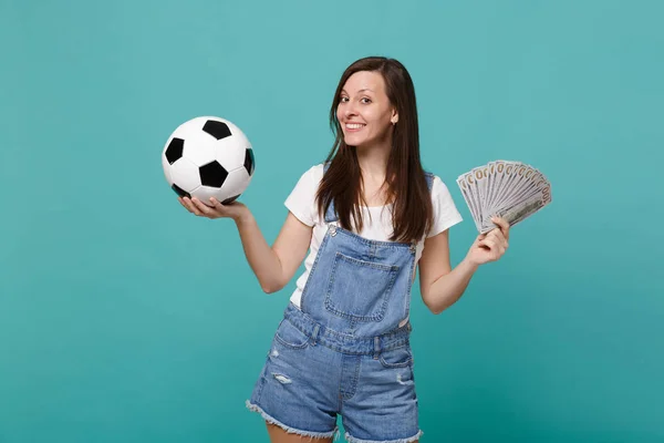 Smiling young woman football fan support favorite team with soccer ball, fan of money in dollar banknotes, cash money isolated on blue turquoise background. Sport family leisure lifestyle concept