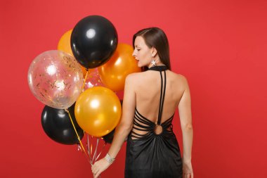 Arkadan bir kenara hava balonları izole kırmızı zemin üzerine tutarak seyir kutluyor küçük siyah elbiseli Genç kızın arka görünümü. St. Valentine's gün mutlu yeni yıl, Doğum günü mockup tatil parti konsept