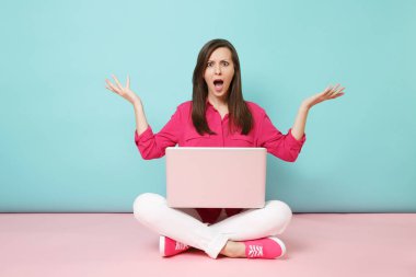 Full length portrait of young woman in rose shirt blouse white pants sitting on floor using laptop pc isolated on pink blue pastel wall background studio. Fashion lifestyle concept Mock up copy space clipart