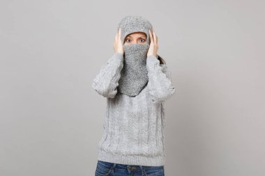 Genç kadın eşarp ile yüzünü kaplayan gri kazak kaydırma gri arka plan üzerinde izole baş el koydu. Sağlıklı moda yaşam tarzı insanların samimi duygular, soğuk sezon kavramı. Kopyalama alanı alay