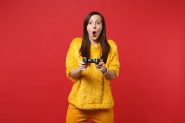 Parlak kırmızı duvar arka plan üzerinde izole joystick ile bilgisayar oyunu oynamak genç kadın ağzı açık, tutarak sarı kürk kazaklı hayran. İnsanlar samimi duygular, yaşam kavramı. Kopyalama alanı alay
