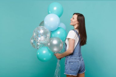 Dikiz neşeli genç kadın bir kenara arıyorum, kutlama, izole mavi turkuaz arka plan üzerinde renkli hava balonları bekletme denim giysileri geri. Doğum günü tatil partisi, insanların duyguları kavramı