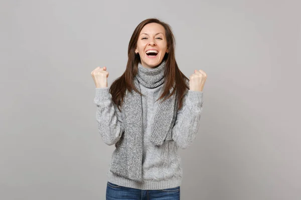 笑着的年轻女子在灰色毛衣 围巾紧握拳头像获胜者隔离在灰色的墙壁背景 健康时尚的生活方式 人真诚的情感 寒冷的季节理念 模拟复制空间 — 图库照片