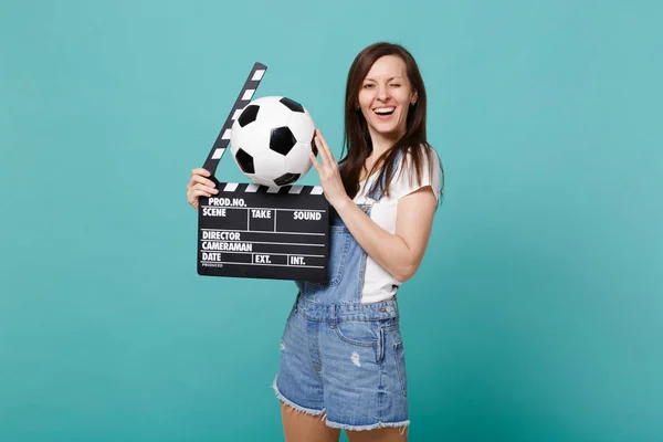 Funny blinking woman football fan support favorite team with soccer ball, classic black film making clapperboard isolated on blue turquoise background. People emotions, sport family leisure concept