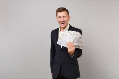 Genç iş adamı klasik siyah elbiseli gülüyor, gömlek holding çok gri arka plan üzerinde izole dolarlık banknotlar nakit para demet. Başarı kariyer servet iş kavramı. Kopyalama alanı alay