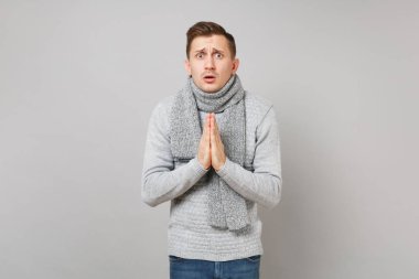 Gri süveterli birlikte, el ele tutuşarak eşarp genç adam yalvaran dua gri duvar arka plan üzerinde izole. Sağlıklı moda yaşam tarzı, insanlar samimi duygular, soğuk sezon kavramı. Kopyalama alanı alay