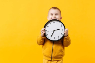 Küçük çocuk çocuk 3-4 yıl sarı elbise giyen eski turuncu duvar arka planda, çocuk stüdyo portre izole saat tutun. İnsanlar samimi duygular, çocukluk yaşam tarzı kavramı. Kopyalama alanı alay