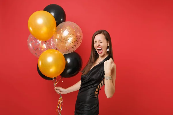 Mutlu genç kız küçük siyah elbise kutlayarak hava balonları izole kırmızı zemin üzerine tutarak kazanan jest yapıyor. Uluslararası kadın gün Happy New Year doğum günü mockup tatil parti konsept. — Stok fotoğraf