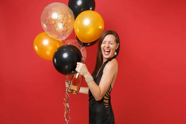 Šťastná mladá žena v černých šatech slaví křik drží láhev šampaňského s vrtulovým pohonem izolované na červeném pozadí. Mezinárodní Dámské den šťastný nový rok narozeniny maketa holiday party koncept. — Stock fotografie