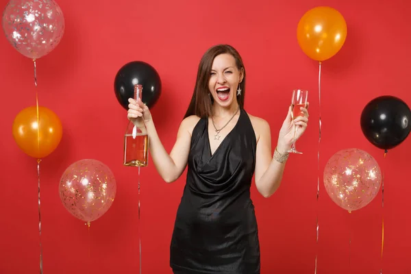 Jovem alegre em pouco vestido preto celebrando segurando vidro, garrafa de champanhe em balões de ar de fundo vermelho brilhante. Dia dos Namorados, Feliz Ano Novo, conceito de festa de aniversário mockup . — Fotografia de Stock