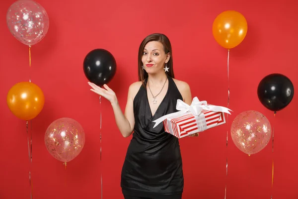 被弄伤的女孩穿着黑色的衣服摊开双手 拿着红色的盒子和礼物 呈现在鲜红的背景气球上 女儿节 新年快乐 生日模拟节日派对理念 — 图库照片