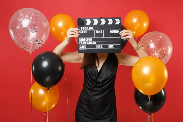 Jeune fille en petite robe noire couvrant visage avec film noir classique faisant clapperboard sur fond rouge vif ballon à air. Saint Valentin, Bonne année, concept de fête de fête anniversaire maquette . — Photo