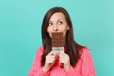 Örgü pembe kazaklı bakılması, dalgın genç kadın elinde, mavi duvar arka planda, stüdyo portre izole çikolata ile ağız kapsayan tutun. İnsanlar yaşam tarzı kavramı. Kopyalama alanı alay
