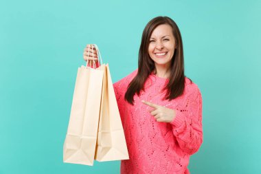 Örgü pembe kazaklı işaret parmağı paketleri çanta üzerinde mavi arka plan izole elinde alışveriş sonra satın almalarla üzerinde gülümseyen genç kadın. İnsanlar yaşam tarzı kavramı. Kopyalama alanı alay