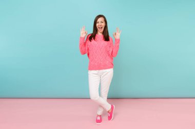 Tam uzunlukta örme gül kazaklı gülümseyen genç kadın portresi, beyaz parlak pembe mavi pastel duvar arka planda Studio izole poz pantolon. Moda yaşam tarzı kavramı. Kopyalama alanı alay