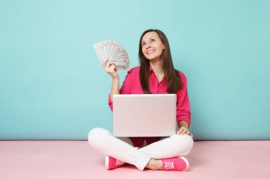 Tam uzunlukta gül gömlek bluz genç kadın portresi, beyaz pantolon katta oturan pembe mavi pastel duvar arka plan studio izole para pc tutun. Moda yaşam tarzı kavramı. Kopyalama alanı alay