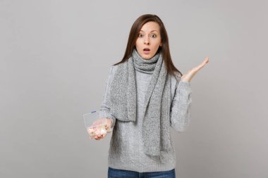 Gri süveterli şok genç kadın eşarp Yayilim eller, her gün hap kutusu gri arka plan üzerinde izole tutmak. Sağlıklı yaşam tarzı, hasta hasta hastalık tedavileri, soğuk sezon kavramı. Kopyalama alanı alay