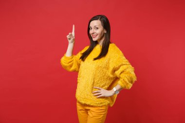 Studio parlak kırmızı duvar zemin üzerine sarı kürk kazaklı işaret parmağı yukarıyı gülümseyen genç ve güzel kadın portresi izole. İnsanlar samimi duygular, yaşam kavramı. Kopyalama alanı alay